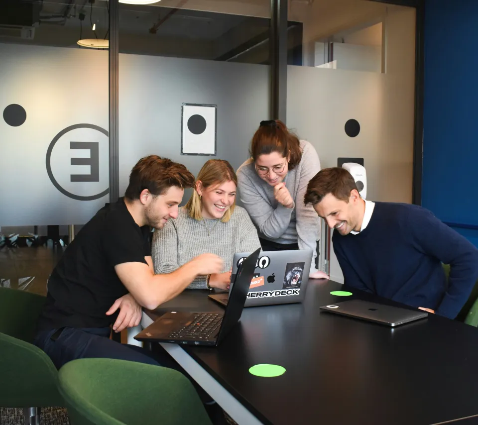 Four people collaborating around laptops during a group meeting.